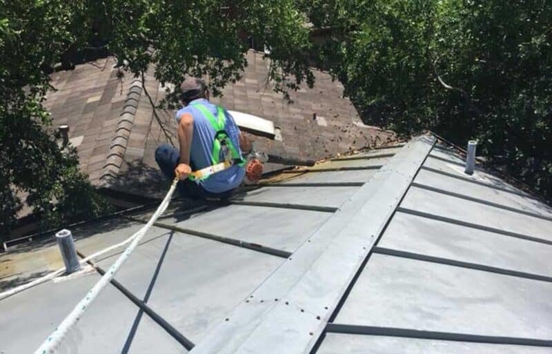 man attached to safety harness blowing leaves off of roof with leaf blower