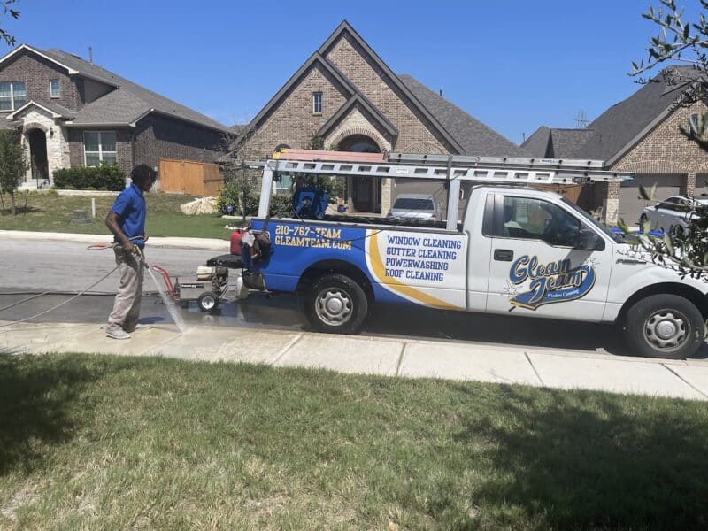 gleam team member cleaning the sidewalk in residential neighborhood with gleam team truck in the background