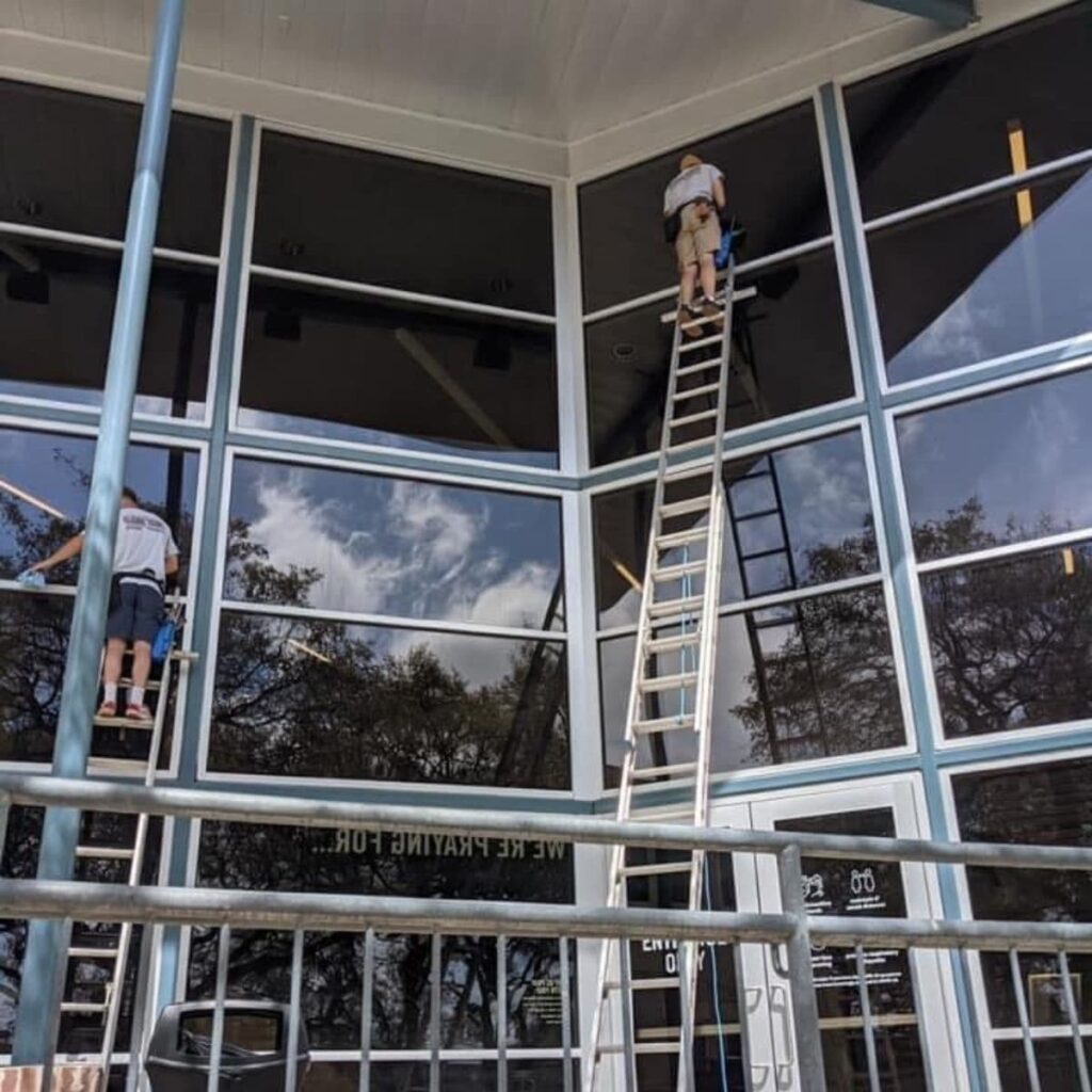 gleam team team members high up on ladders to perform window cleaning services for a commercial building